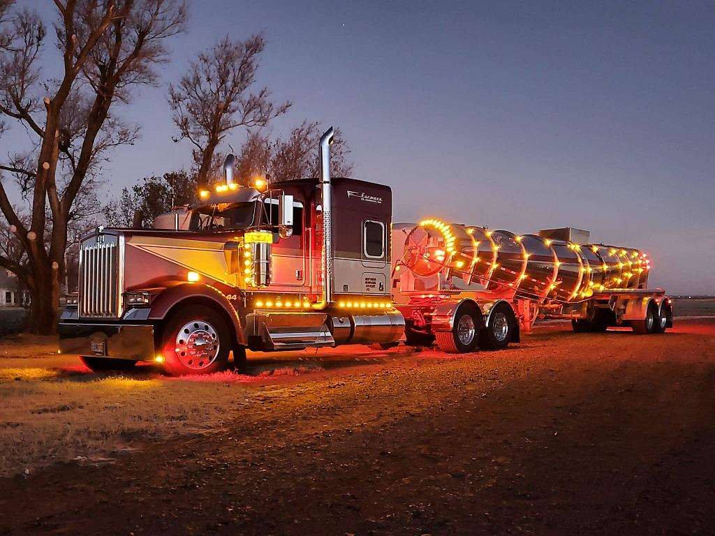 Farmers Oil Kenworth and stainless tanker outlined in amber marker lights at dusk